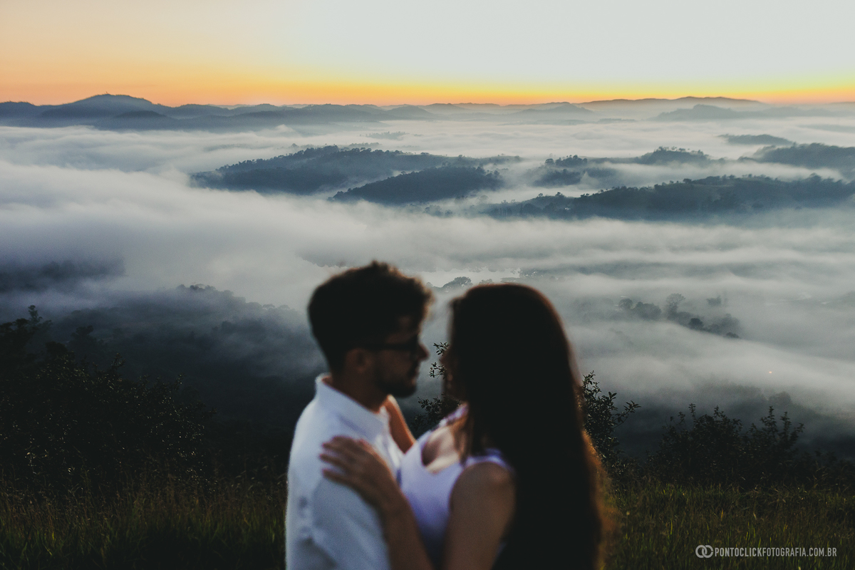 Casal em silhueta no Morro do Capuava em Pirapora do Bom Jesus durante ensaio pré wedding ao nascer do sol com mar de nuvens e paisagem ampla ao fundo criando atmosfera romântica