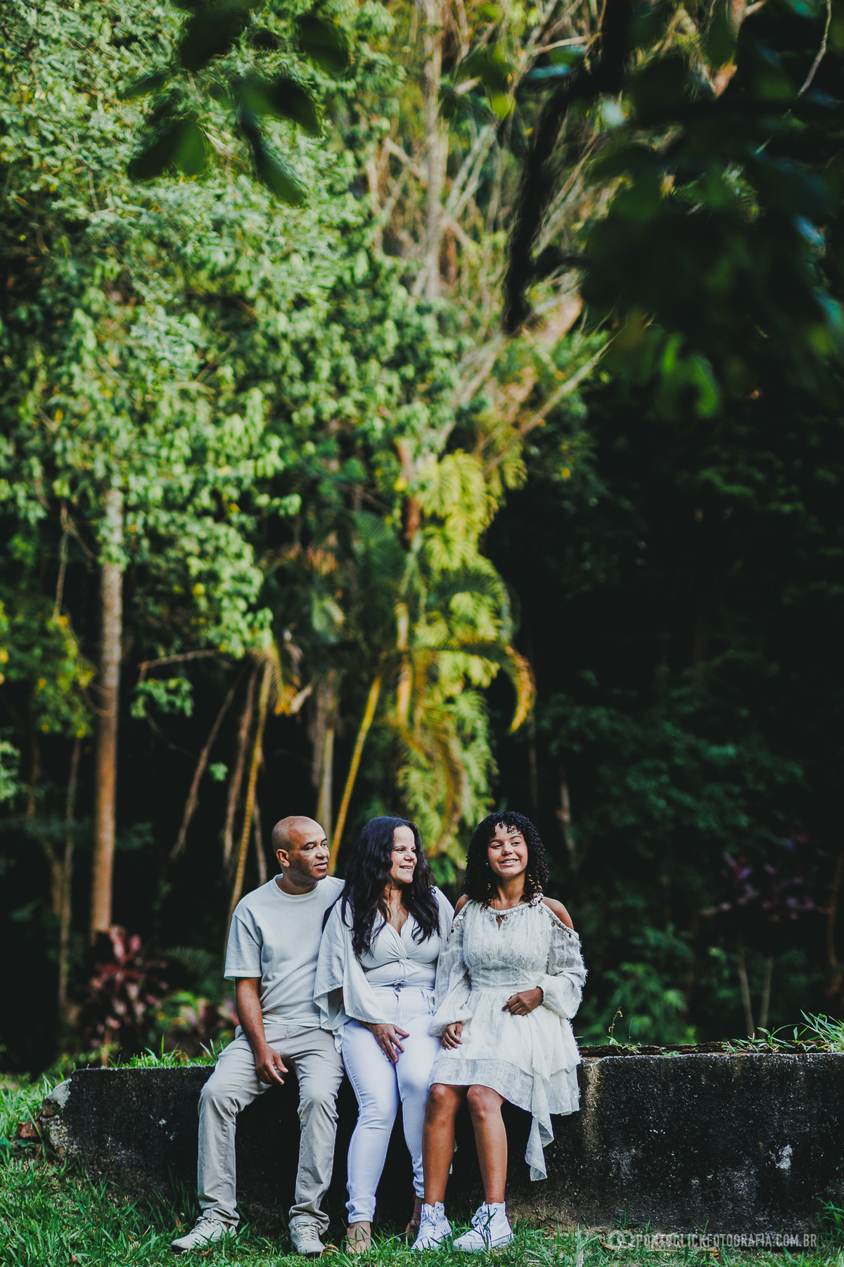 Ensaio de 15 anos em São Roque no Brasital com três pessoas sentadas em área verde cercada pela natureza, em fotografia espontânea com composição ampla, transmitindo conexão, leveza e momento especial durante o ensaio externo