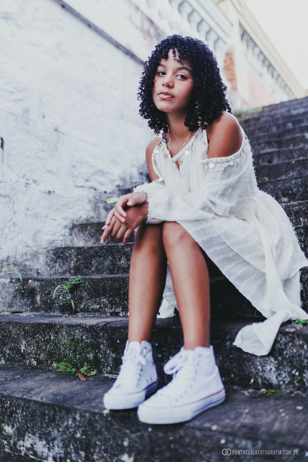 Retrato de debutante em ensaio de 15 anos no Brasital em São Roque com jovem sentada em escadaria, usando vestido branco e tênis, em composição urbana elegante que destaca atitude, beleza natural e personalidade
