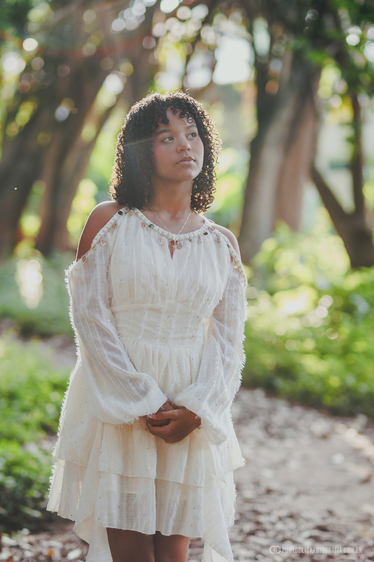 Retrato de 15 anos no Brasital em São Roque com debutante em vestido branco sob luz natural entre árvores, fotografia delicada com fundo verde desfocado, expressão suave e composição romântica que valoriza beleza e feminilidade