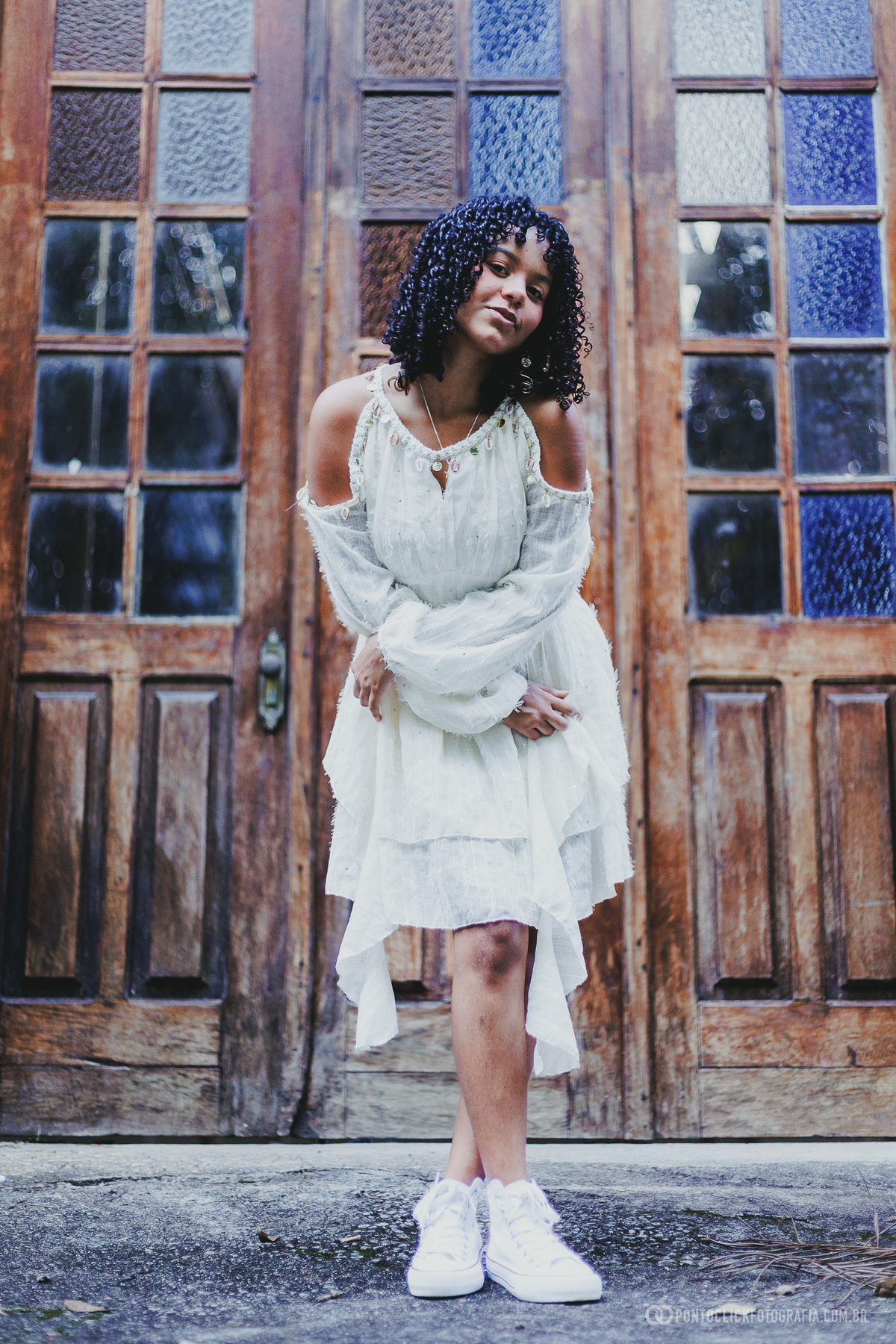 Ensaio de 15 anos em São Roque no Brasital com debutante diante de porta de madeira, usando vestido branco e tênis, em retrato com composição urbana e elegante, valorizando personalidade, estilo e beleza em cenário arquitetônico