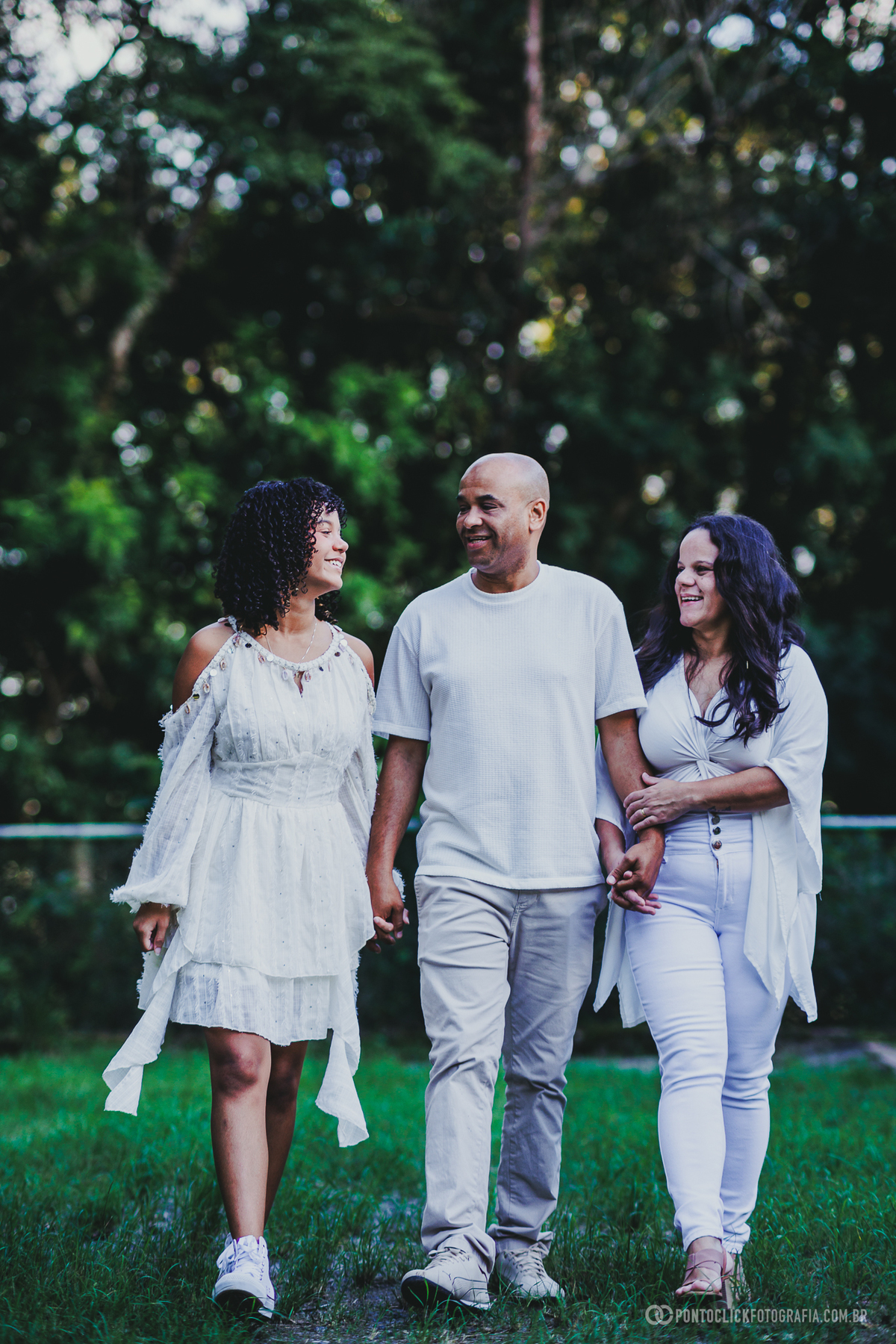 Fotografia de ensaio de 15 anos em São Roque no Brasital com debutante caminhando ao lado de duas pessoas em área verde, em registro espontâneo e afetivo com fundo desfocado, transmitindo conexão, carinho e leveza em momento especial