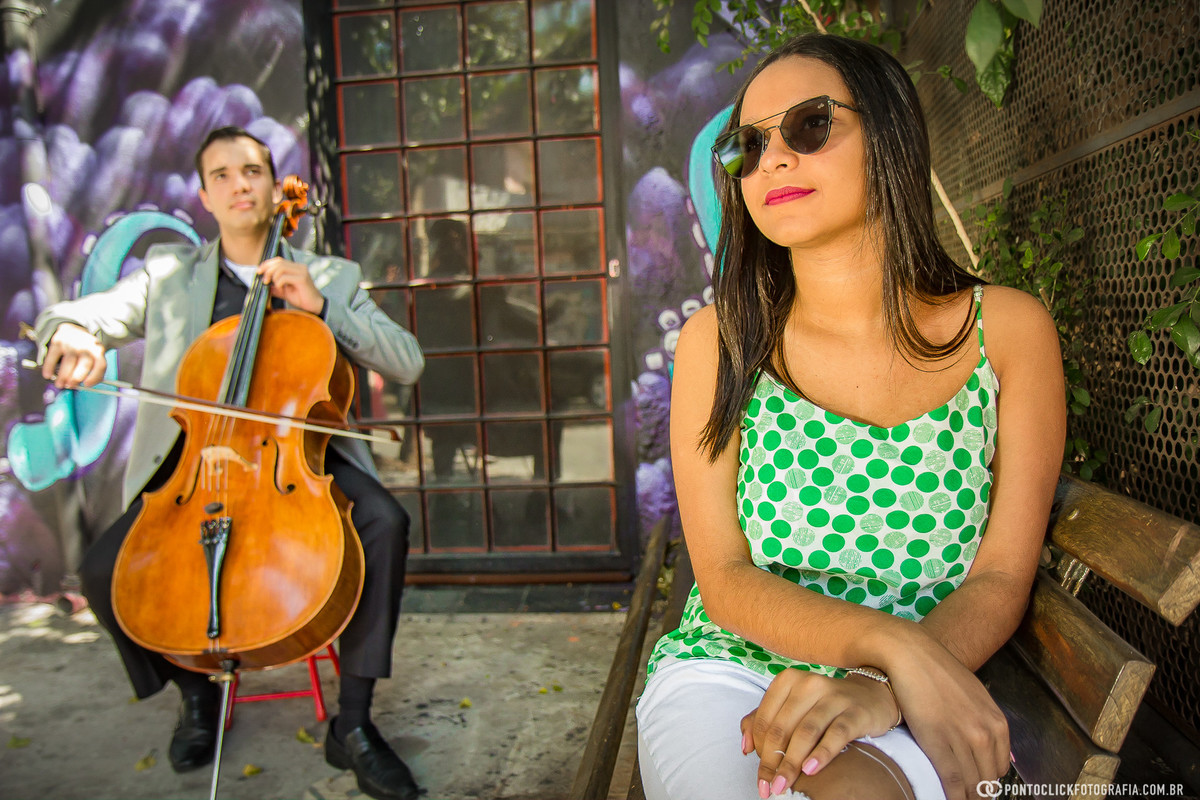 sorrindo e ao fundo um musico tocando violão selo no beco do batman