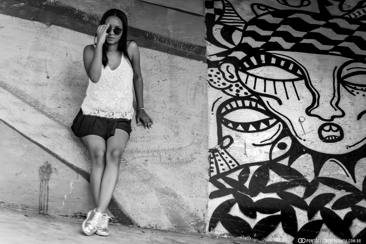 sentada com a mao no oculos e uma pintura no muro da avenida paulista