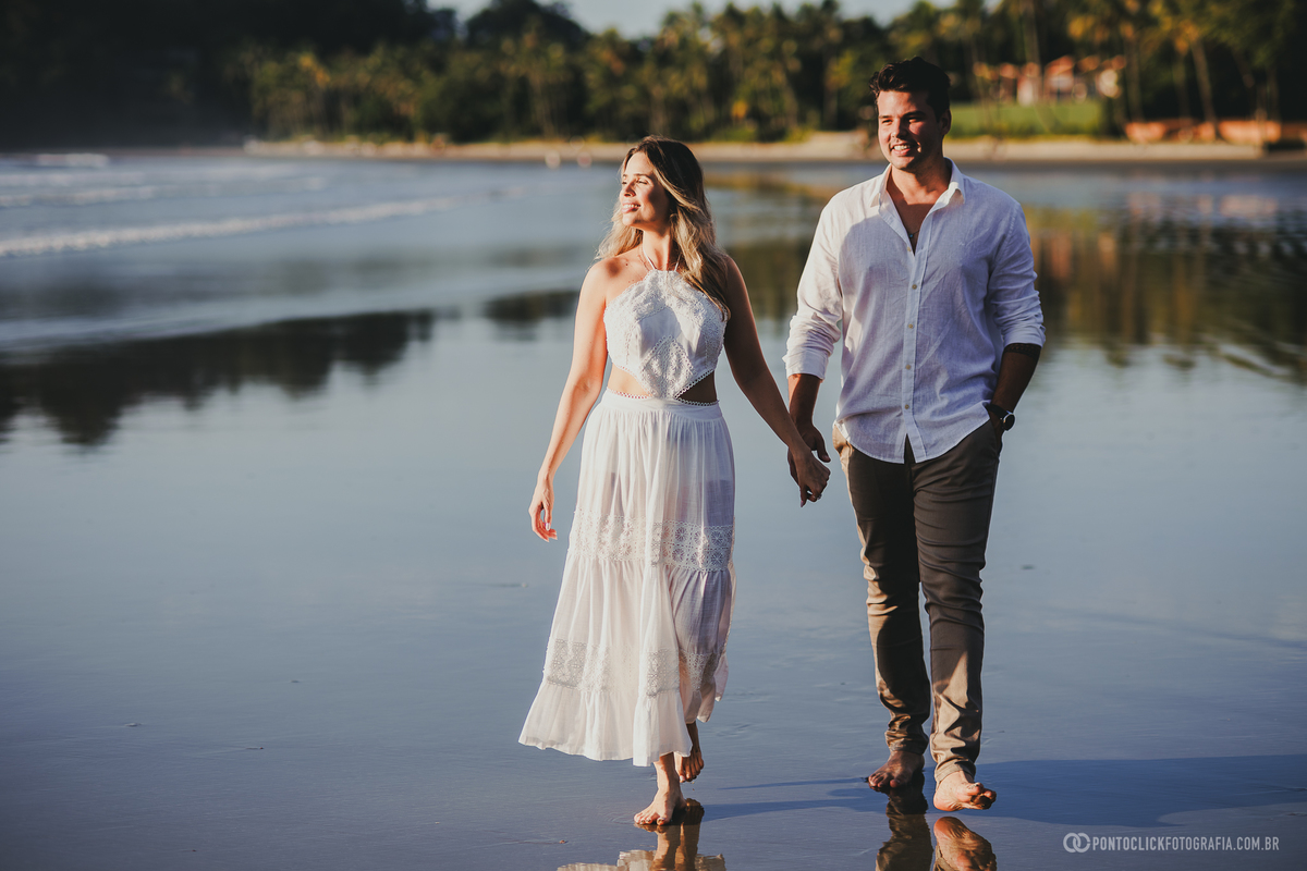 Ensaio pré casamento de Guilherme e Katioska caminhando pela praia do Guarujá ao entardecer, registrando momentos espontâneos, reflexos na areia e conexão natural do casal em cenário paradisíaco