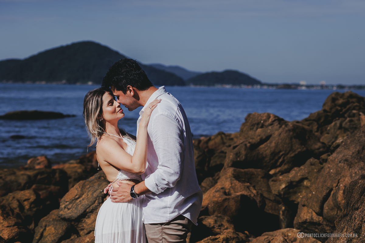 Ensaio pré wedding de Guilherme e Katioska realizado no Guarujá com cenário de pedras e mar ao fundo, registrando momentos românticos do casal em clima leve e natural no litoral paulista ao entardecer