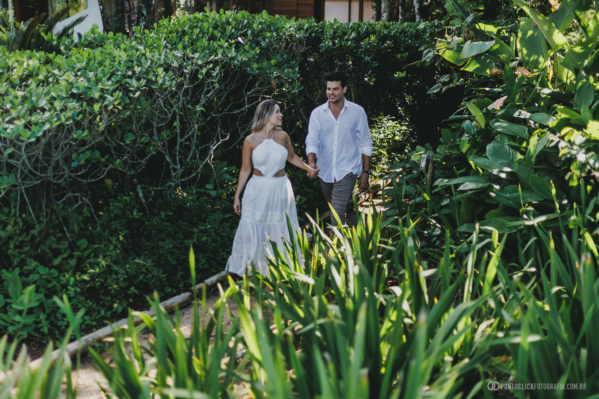Ensaio pré casamento de Guilherme e Katioska caminhando em meio à natureza tropical no Guarujá, registrando momentos espontâneos e românticos do casal em cenário elegante próximo à praia.