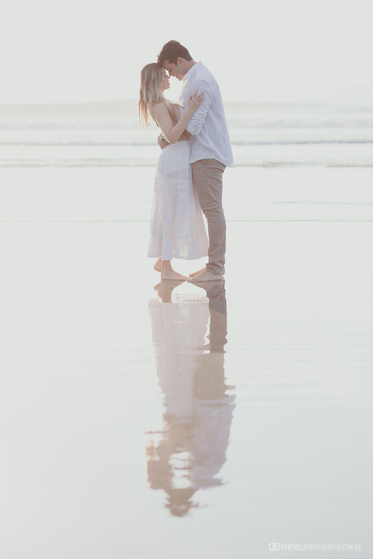 Ensaio pre wedding de Guilherme e Katioska na praia do Guarujá com reflexo na areia e luz suave do fim de tarde, criando cenário romântico e elegante para registrar a conexão e emoção do casal 