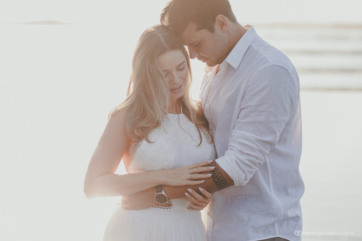 Ensaio fotográfico de casal no Guarujá com Guilherme e Katioska em momento romântico na praia durante o pôr do sol, valorizando luz natural, reflexos na areia e conexão espontânea do casal.