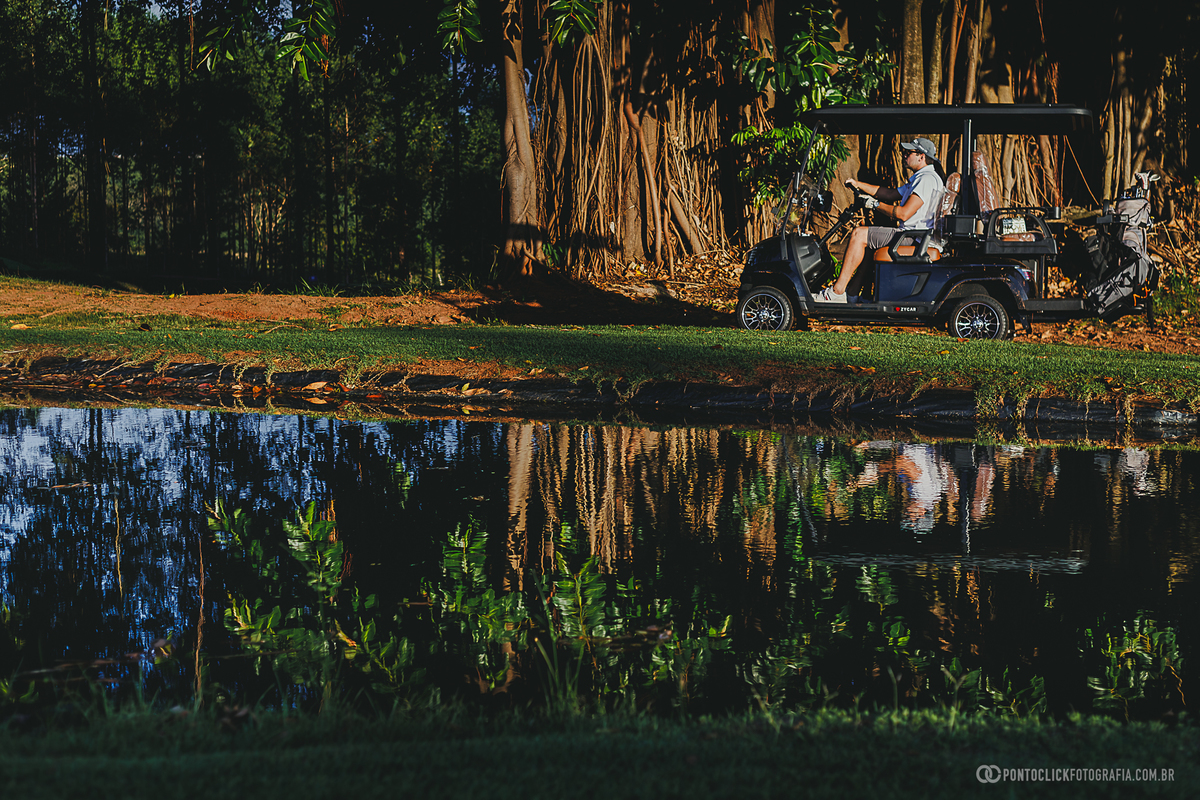 Carrinho de golfe percorre o campo ao lado de um lago durante ensaio fotográfico lifestyle. A composição destaca a paisagem, o ambiente natural e a experiência de registrar momentos em um cenário sofisticado ao ar livre