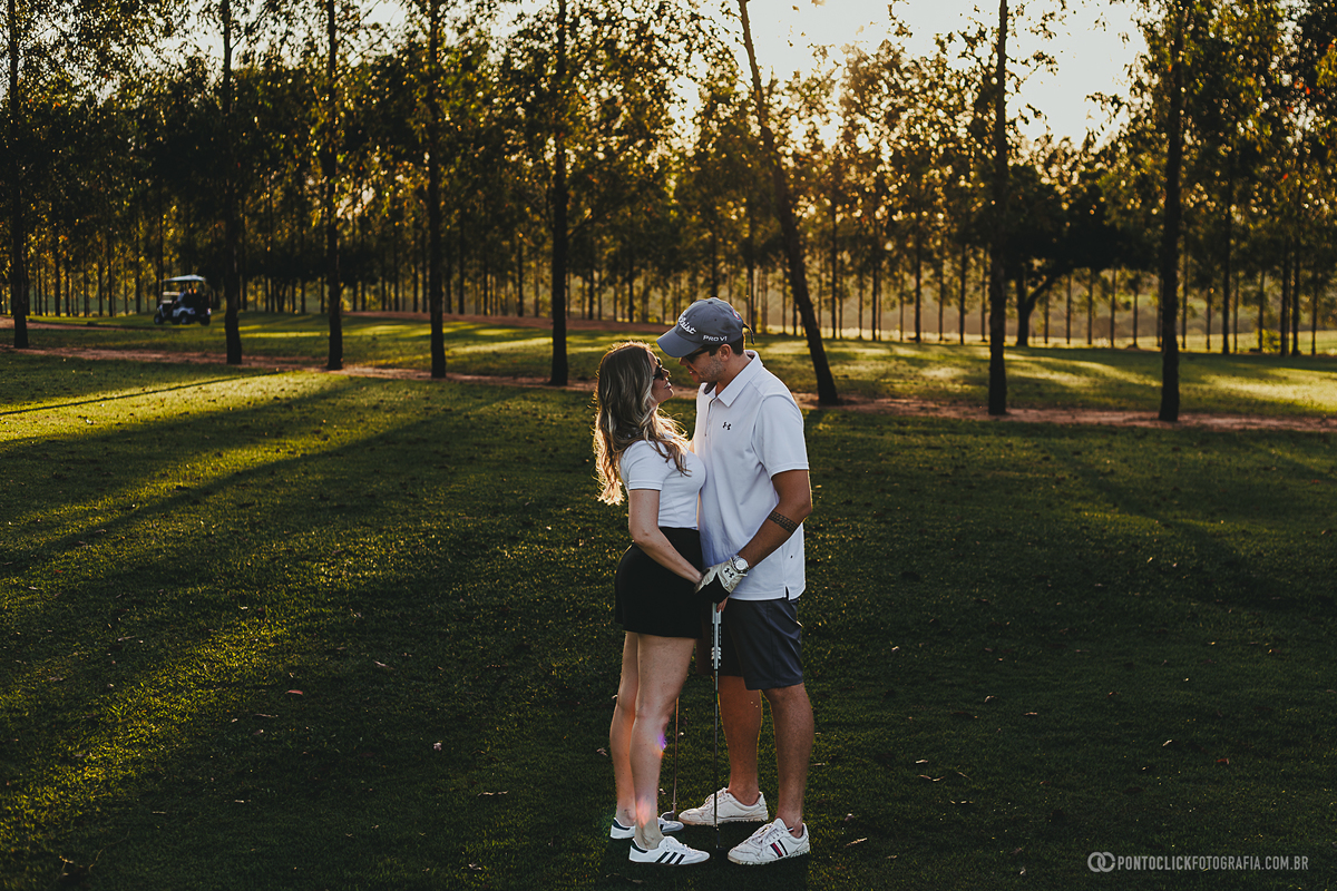 Casal compartilha um olhar cheio de carinho durante ensaio fotográfico em campo de golfe. A fotografia valoriza a conexão do casal, a luz natural e o ambiente ao ar livre, criando registros elegantes e atemporais