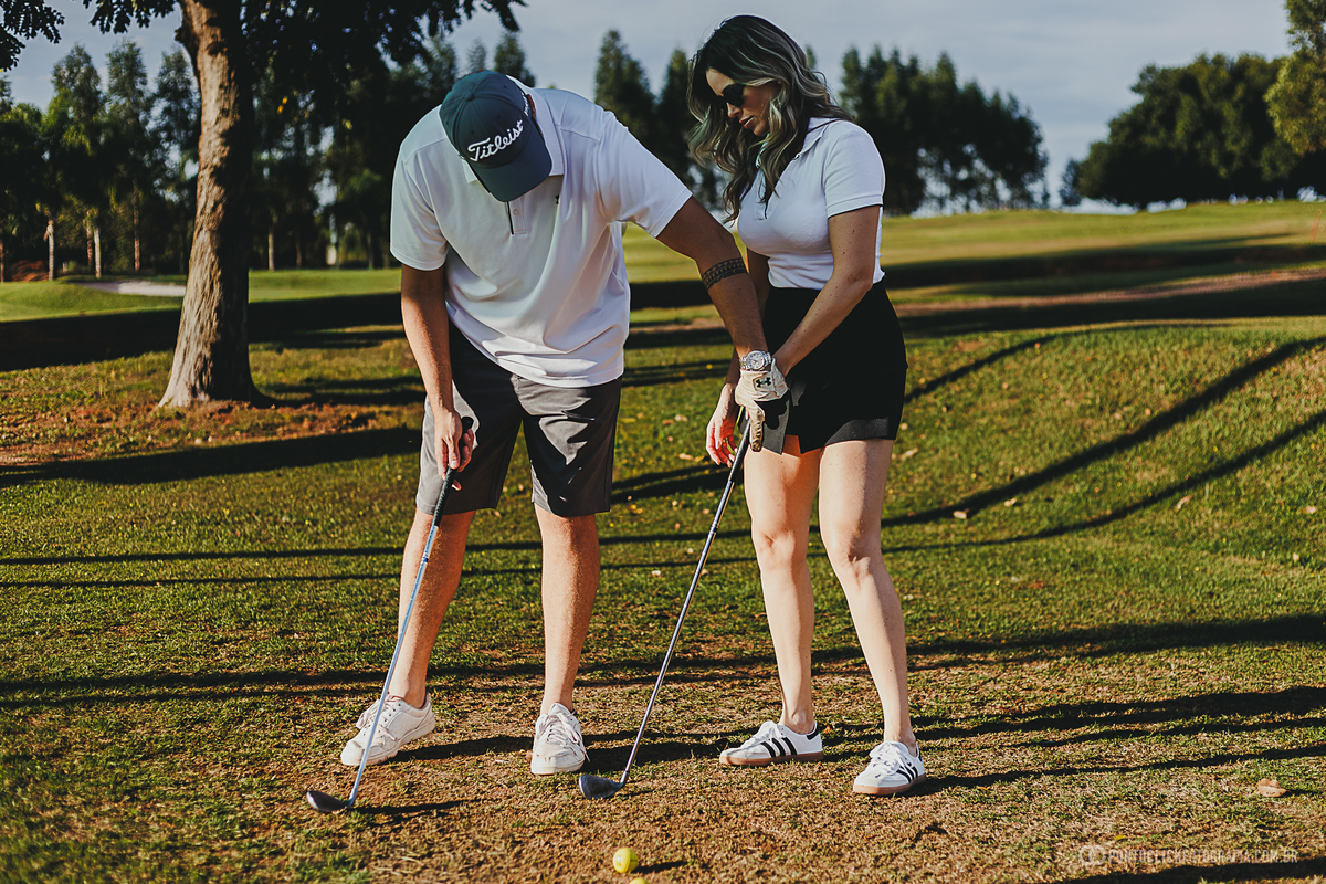 Casal compartilha um momento descontraído durante um ensaio fotográfico em campo de golfe, aprendendo juntos os primeiros movimentos do esporte. A fotografia valoriza cumplicidade, diversão e a beleza dos registros ao ar livre