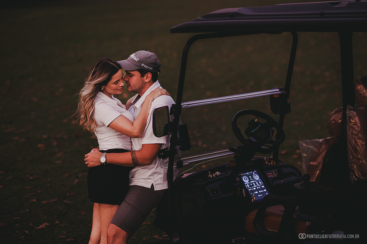 Casal troca um abraço durante ensaio fotográfico ao lado do carrinho de golfe, aproveitando a luz suave do entardecer. A fotografia registra conexão, romantismo e a beleza de um ensaio lifestyle em meio à natureza