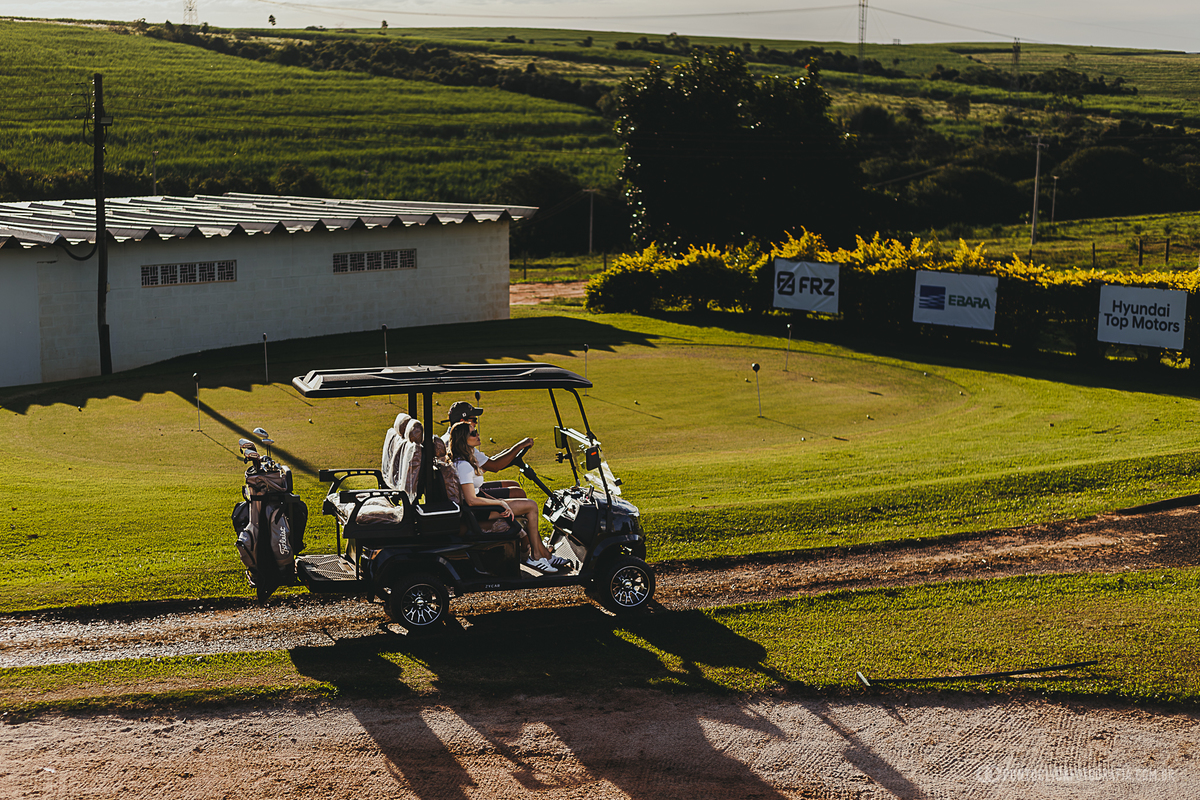 Casal percorre o campo em carrinho de golfe durante um ensaio fotográfico externo, explorando diferentes cenários naturais. A composição evidencia o clima leve, a paisagem e a experiência de um ensaio lifestyle ao ar livre