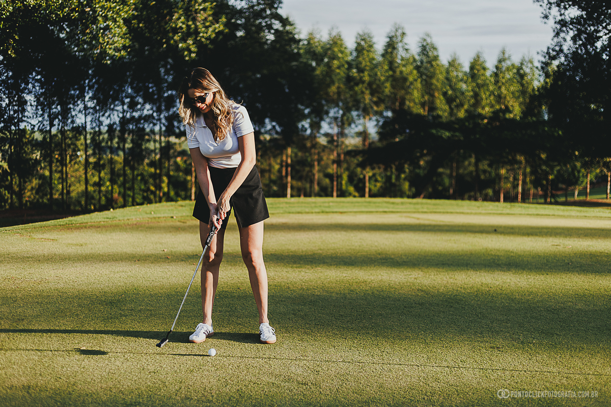 Fotografia registra participante praticando golfe durante ensaio lifestyle em campo aberto. O cenário valoriza o esporte, a natureza e a leveza do momento, criando imagens elegantes para ensaio de casal realizado ao ar livre