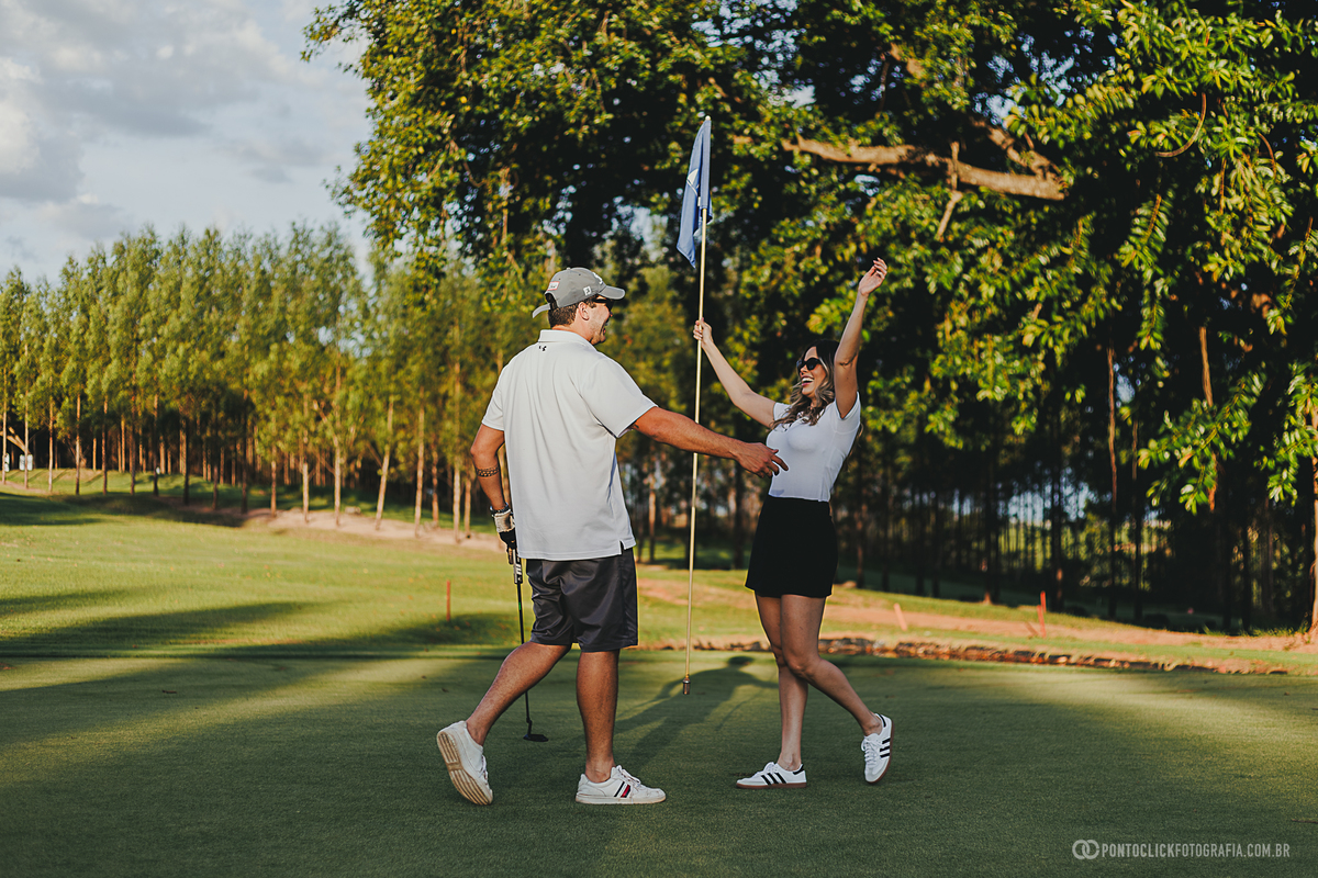 Casal celebra um momento especial durante ensaio fotográfico em campo de golfe, transmitindo alegria e cumplicidade. O registro destaca expressões naturais, cenário verde e a proposta leve de um ensaio lifestyle ao ar livre