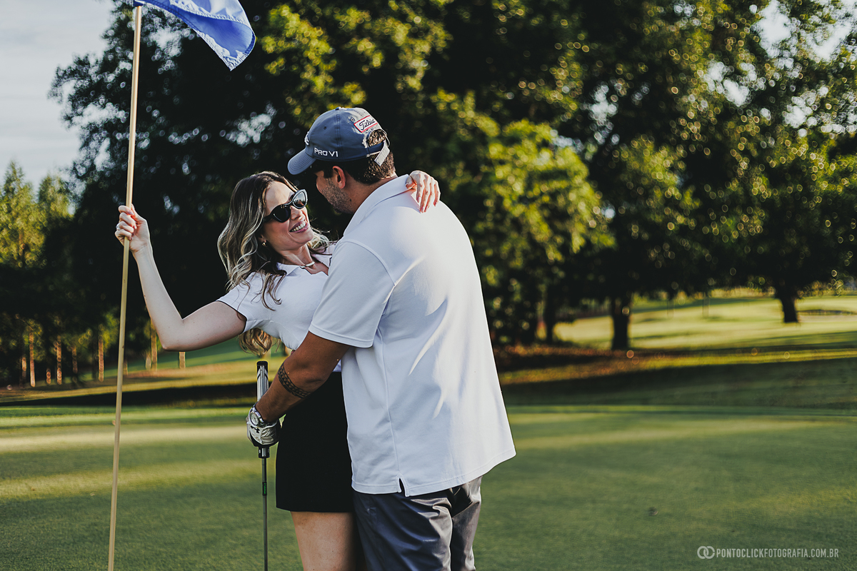 Abraço espontâneo durante ensaio fotográfico de casal em campo de golfe, valorizando conexão, carinho e autenticidade. A fotografia combina natureza, luz natural e um cenário elegante para registrar momentos inesquecíveis