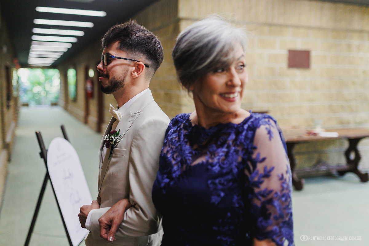 Noivo e mãe aguardam juntos o início da cerimônia, compartilhando um momento de alegria e expectativa antes da entrada na igreja. Fotógrafo de casamento Pontoclick Fotografia.