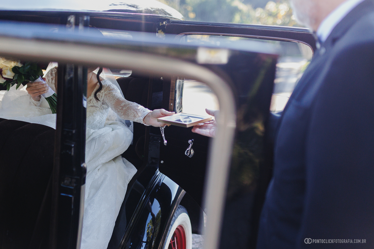 Antes de entrar na igreja, a noiva recebe das mãos do pai um porta-retrato com uma lembrança especial, tornando esse instante ainda mais emocionante. Fotógrafo de casamento Pontoclick Fotografia.