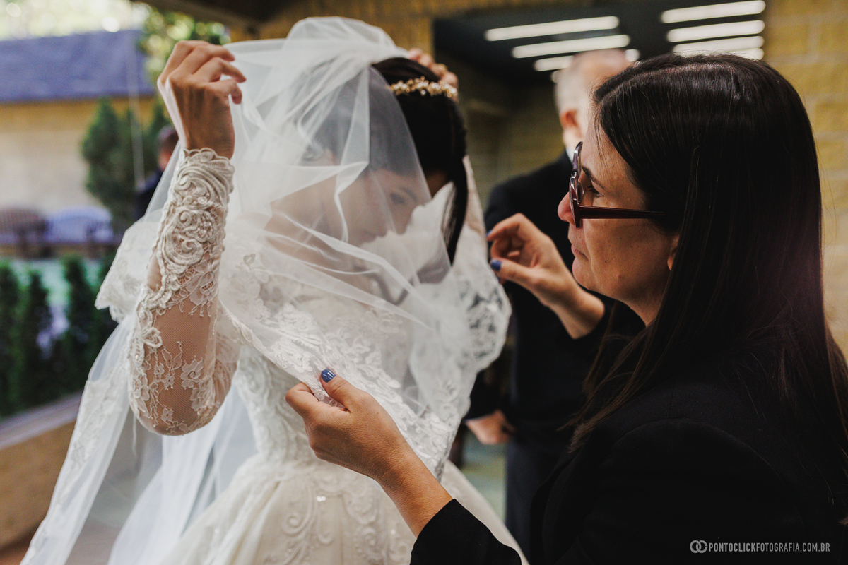 A noiva recebe os últimos ajustes no véu antes de entrar na cerimônia, garantindo que cada detalhe esteja perfeito para o casamento. Fotógrafo de casamento Pontoclick Fotografia.