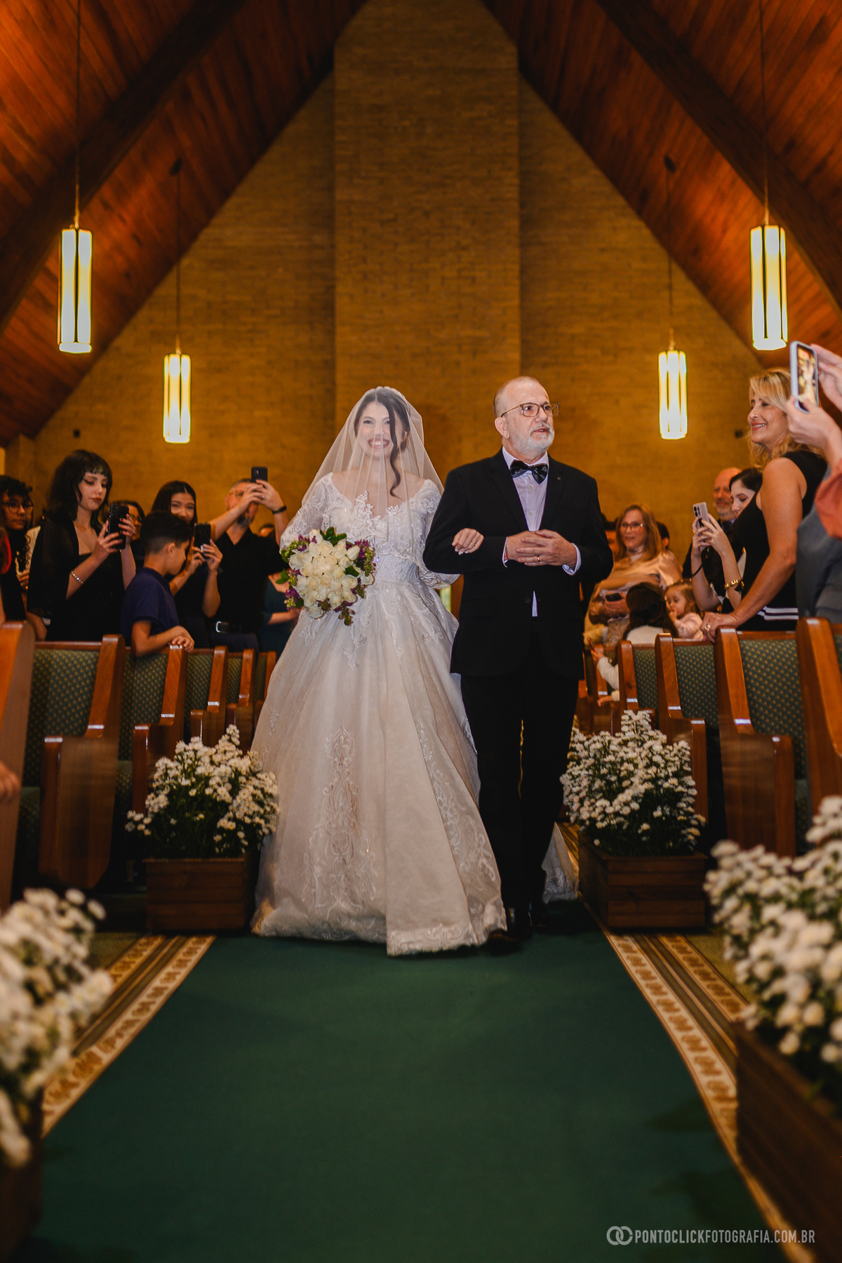 A noiva caminha em direção ao altar durante a cerimônia de casamento, cercada pelo carinho dos convidados e pela emoção desse momento único. Fotógrafo de casamento Pontoclick Fotografia.