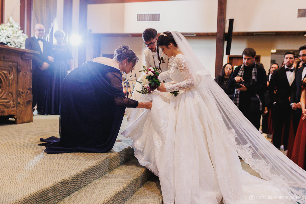 Os últimos detalhes do vestido da noiva são ajustados antes do início da cerimônia, garantindo que tudo esteja perfeito para esse momento especial. Fotógrafo de casamento Pontoclick Fotografia.