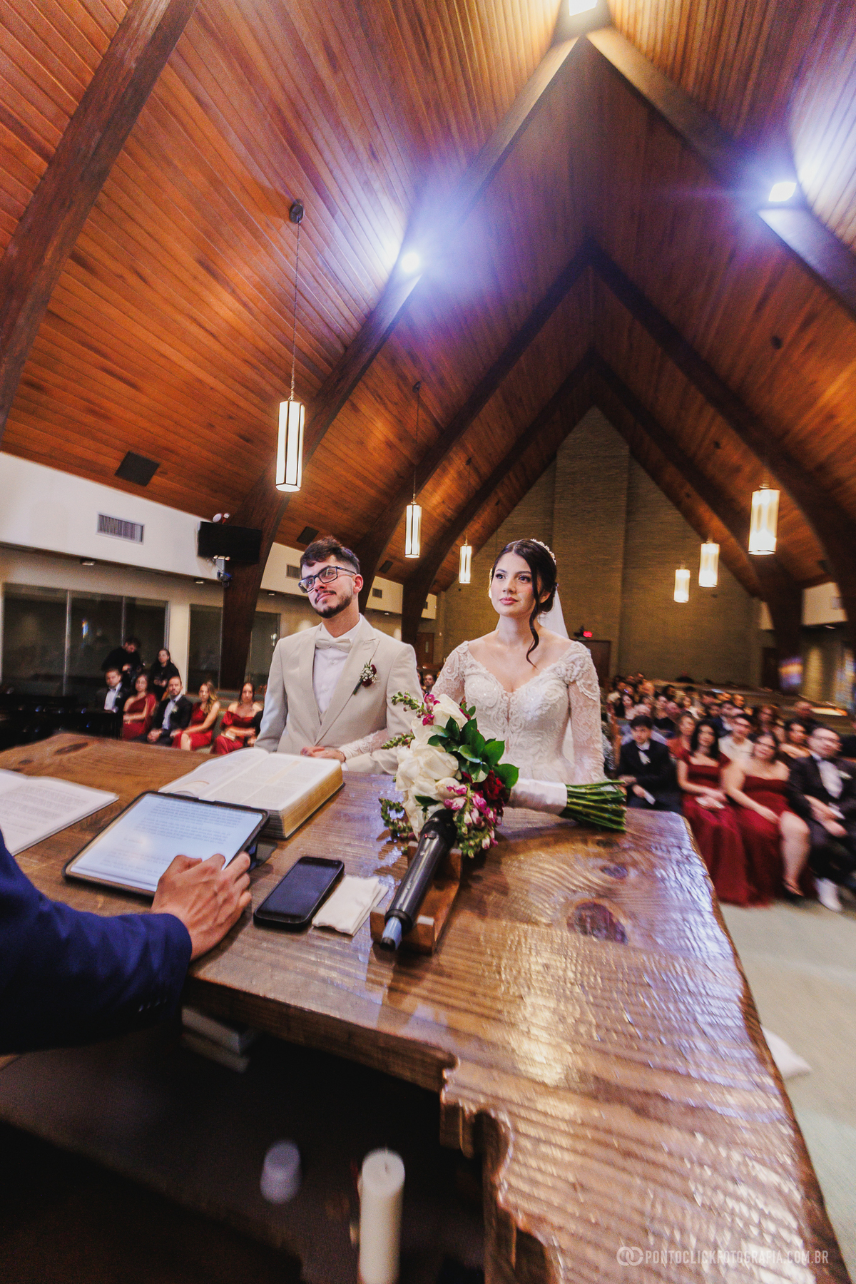Os noivos acompanham a celebração diante do altar durante a cerimônia religiosa, em um registro elegante e atemporal do casamento. Fotógrafo de casamento Pontoclick Fotografia.