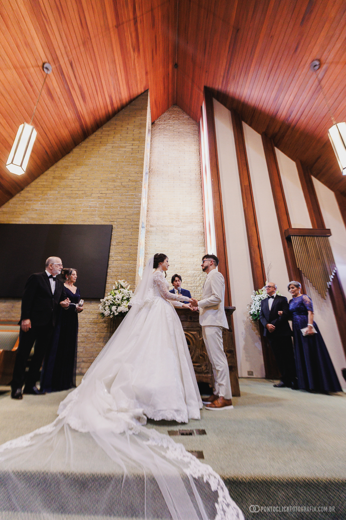 Os noivos permanecem de mãos dadas diante do altar durante a cerimônia, simbolizando a união e o início de uma nova história juntos. Fotógrafo de casamento Pontoclick Fotografia.