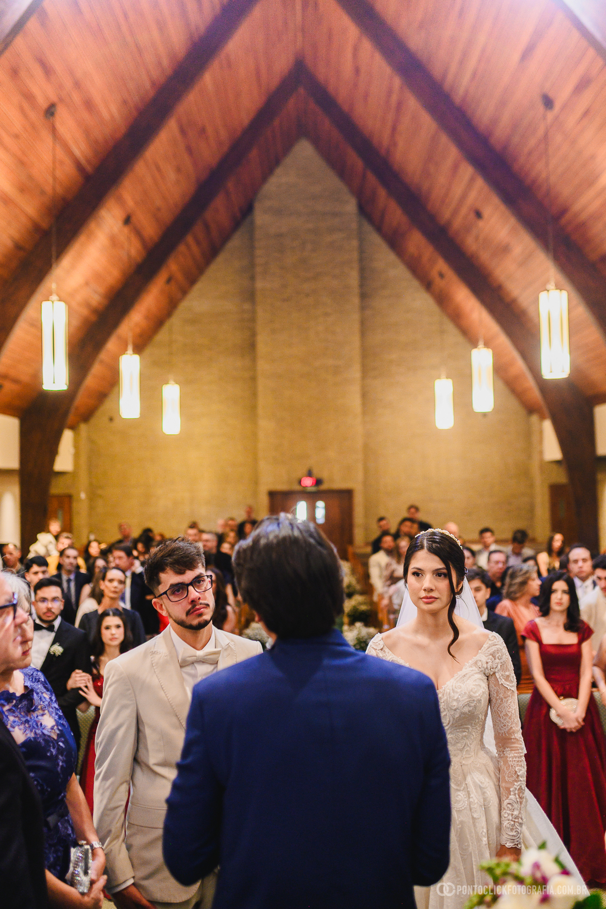 Os noivos acompanham atentamente a mensagem durante a cerimônia religiosa, vivendo um momento de reflexão e significado diante dos convidados. Fotógrafo de casamento Pontoclick Fotografia.
