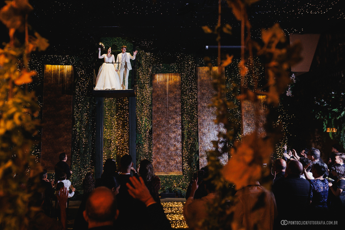 Os noivos fazem sua entrada triunfal na recepção, sendo recebidos com entusiasmo pelos convidados em um momento marcante da festa de casamento. Fotógrafo de casamento Pontoclick Fotografia.