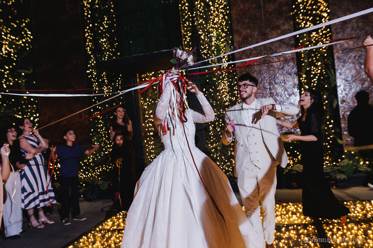Os noivos participam da brincadeira das fitas do buquê durante a festa, compartilhando diversão e interação com os convidados. Fotógrafo de casamento Pontoclick Fotografia.