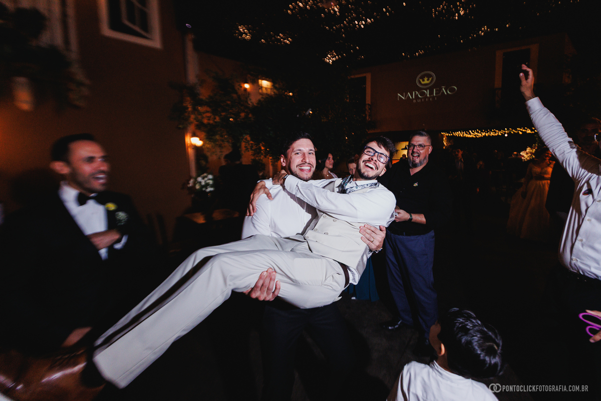 Amigos levantam o noivo durante a festa de casamento, criando um registro espontâneo, divertido e cheio de energia na pista de celebração. Fotógrafo de casamento Pontoclick Fotografia.