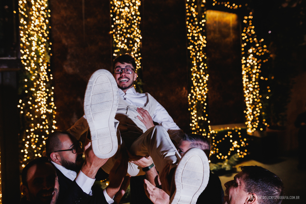 O noivo é erguido pelos amigos durante a festa, vivendo um dos momentos mais descontraídos e animados da recepção de casamento. Fotógrafo de casamento Pontoclick Fotografia.