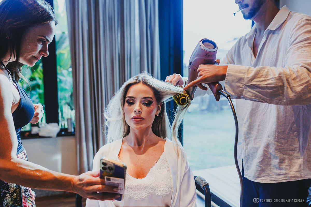 A noiva recebe cuidados no cabelo e na maquiagem ao mesmo tempo, em um registro dos detalhes do seu making of. Fotógrafo de casamento Pontoclick Fotografia.