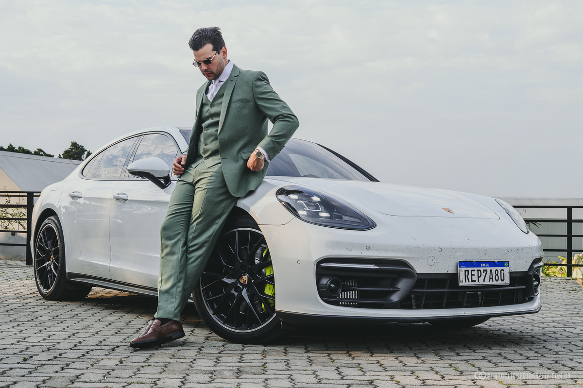 O noivo de terno verde posa ao lado de um Porsche branco antes da cerimônia de casamento. Fotógrafo de casamento Pontoclick Fotografia.
