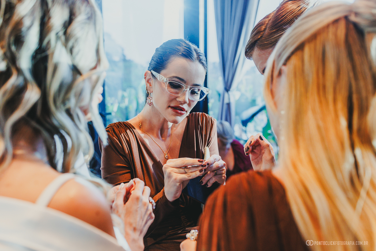Uma madrinha examina um acessório enquanto a noiva e outras convidadas acompanham o momento no making of. Fotógrafo de casamento Pontoclick Fotografia.