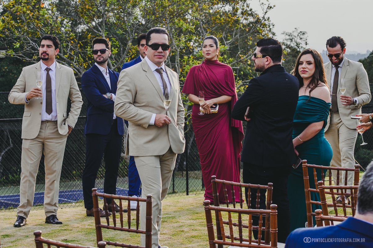Homens de terno claro e convidadas se reúnem ao ar livre antes da cerimônia de casamento. Fotógrafo de casamento Pontoclick Fotografia.