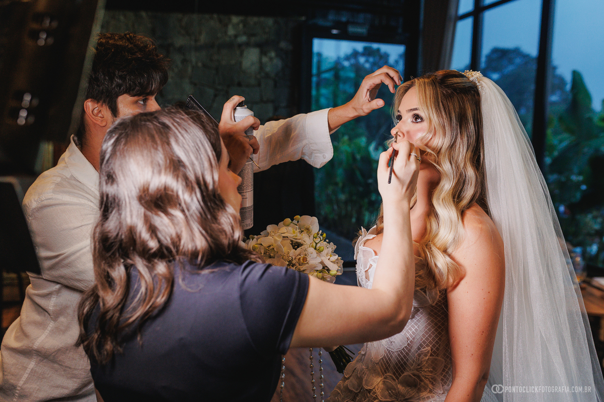 A noiva recebe os últimos retoques de maquiagem e cabelo, já com vestido, véu e buquê. Fotógrafo de casamento Pontoclick Fotografia