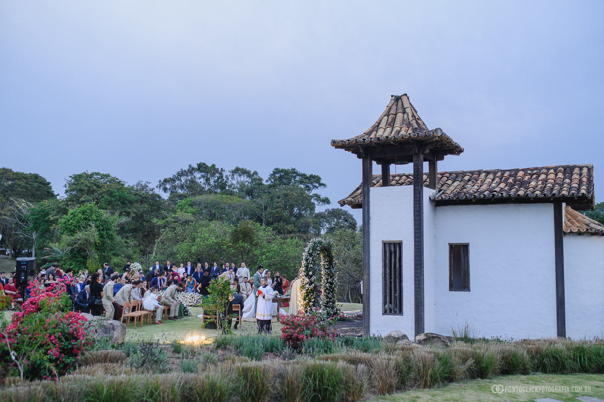 Vista ampla da cerimônia de casamento ao ar livre, com convidados, flores e uma capela ao lado. Fotógrafo de casamento Pontoclick Fotografia.