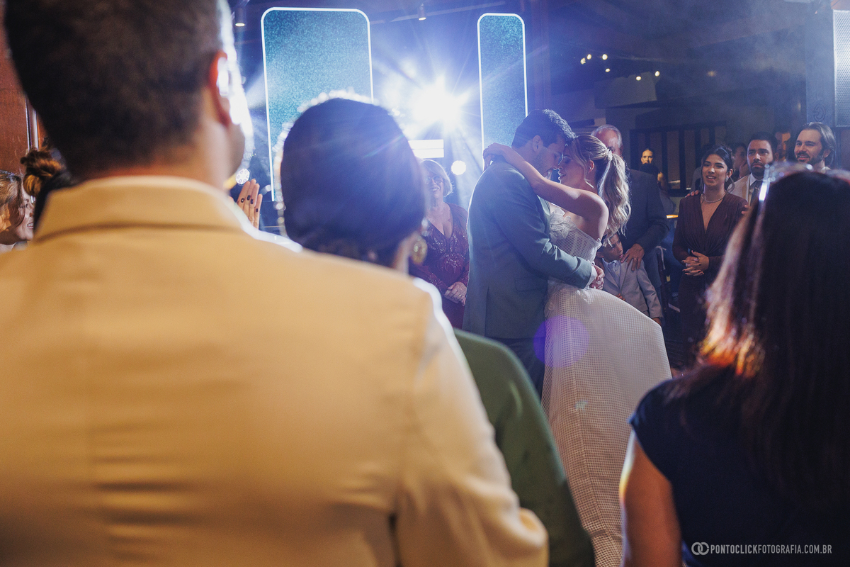 Os noivos dançam abraçados na recepção, cercados pelos convidados e pelas luzes da festa. Fotógrafo de casamento Pontoclick Fotografia