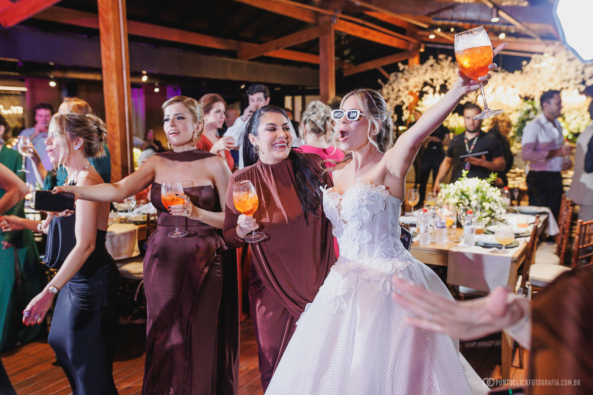 A noiva ergue a taça ao lado de convidadas enquanto todos celebram na pista de dança. Fotógrafo de casamento Pontoclick Fotografia.