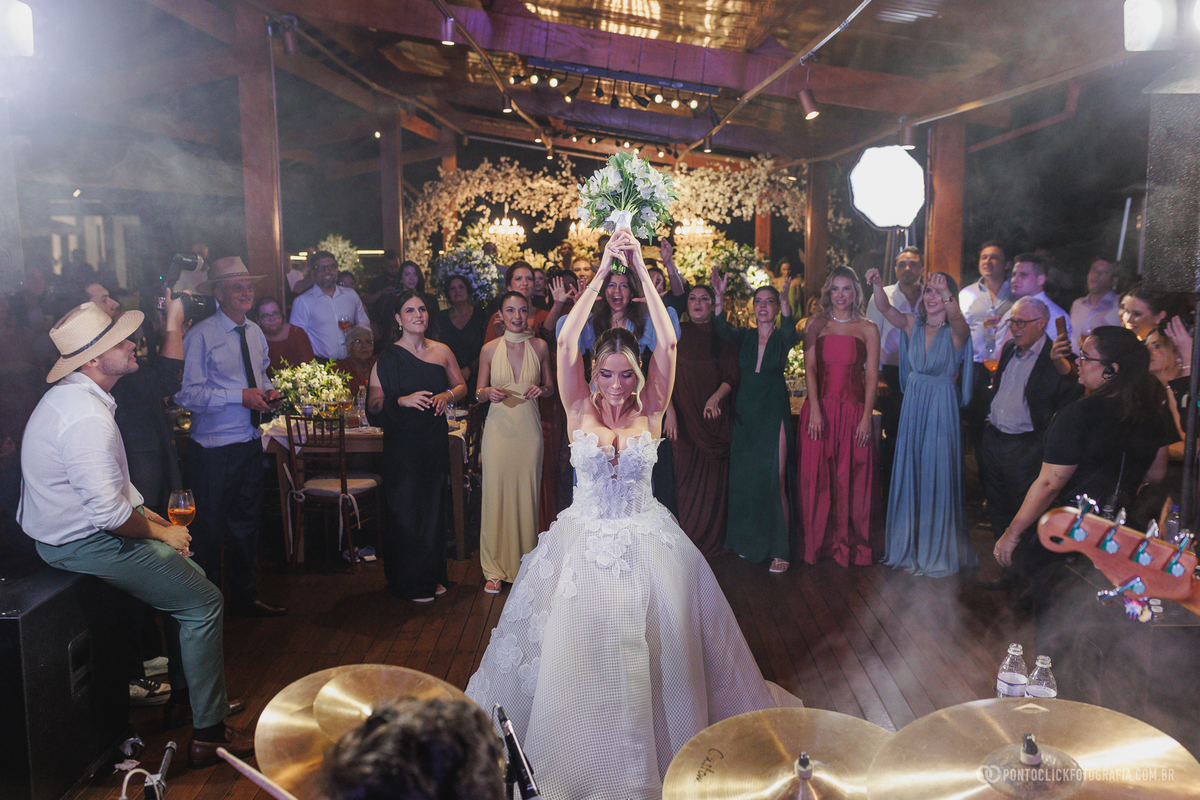 A noiva ergue o buquê diante de um grupo de convidadas durante a festa de casamento. Fotógrafo de casamento Pontoclick Fotografia.