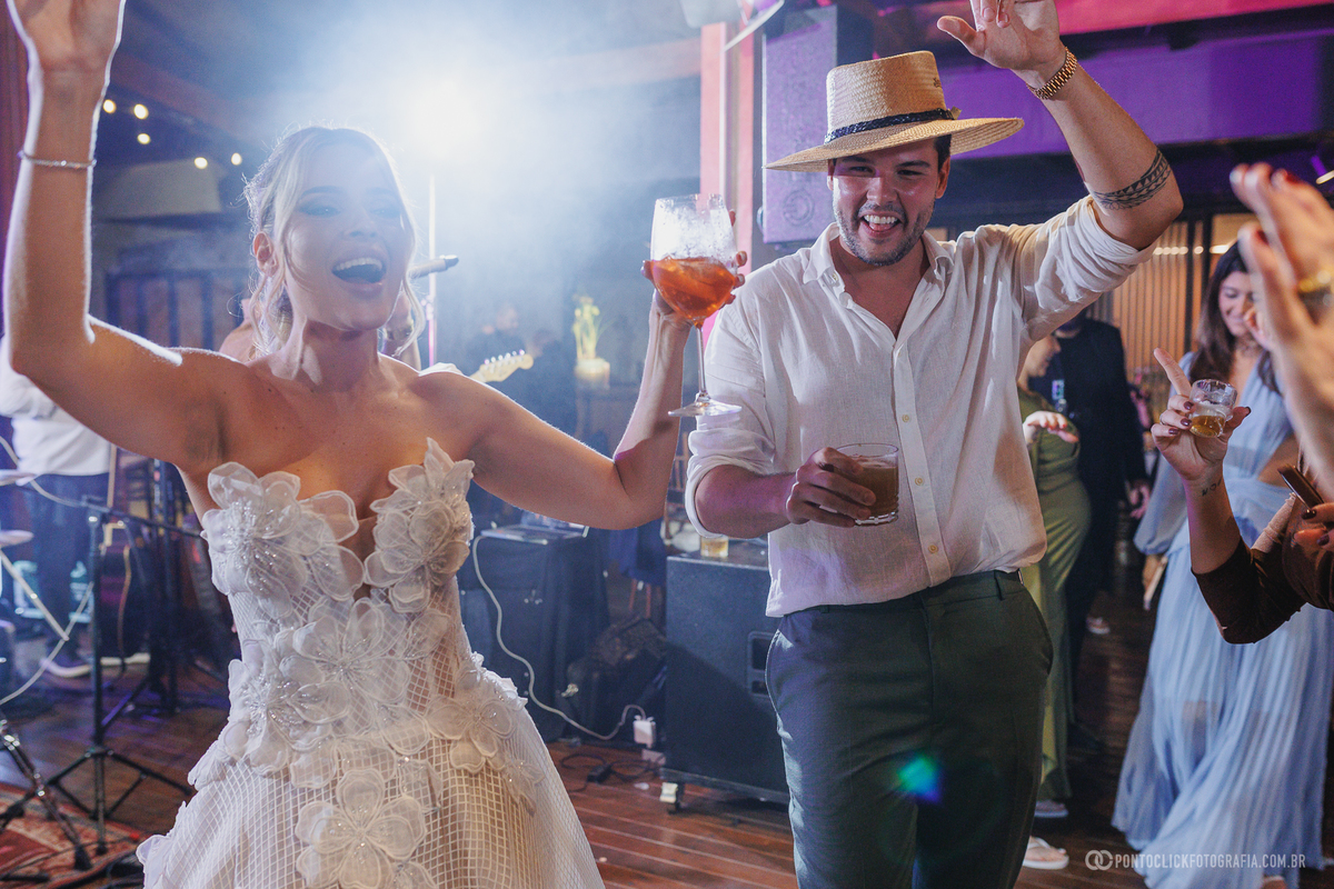 A noiva dança com uma taça na mão ao lado de um convidado de chapéu. Fotógrafo de casamento Pontoclick Fotografia.