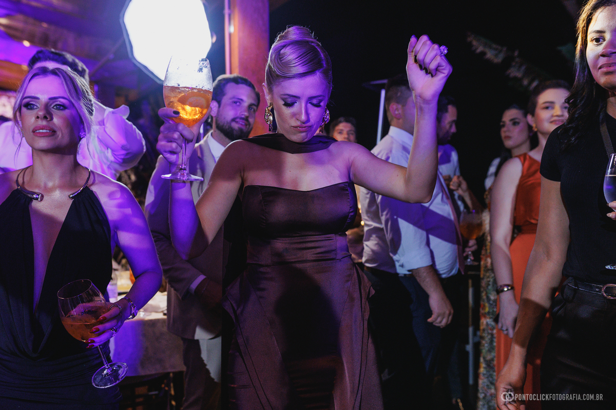 Convidadas dançam e erguem suas taças sob as luzes coloridas da festa de casamento. Fotógrafo de casamento Pontoclick Fotografia.