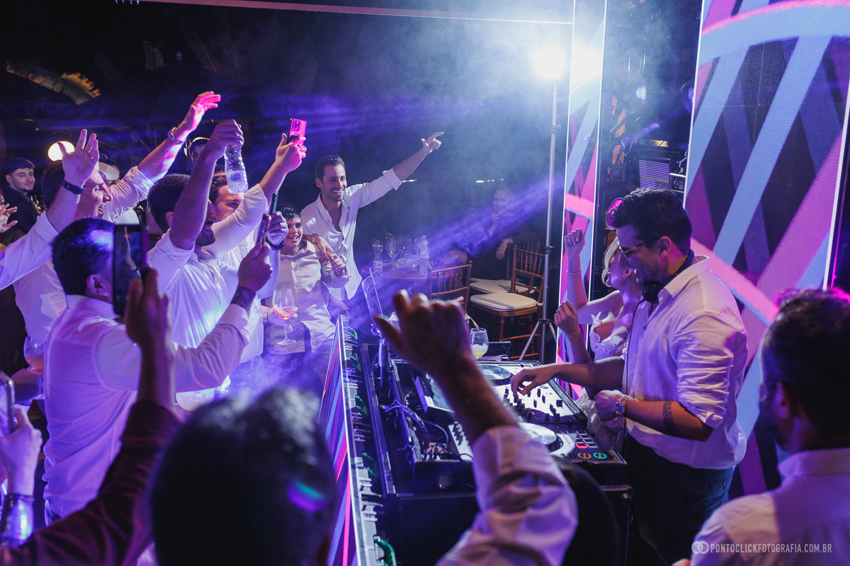 Convidados celebram ao redor do DJ, com braços erguidos e celulares registrando a festa de casamento. Fotógrafo de casamento Pontoclick Fotografia.