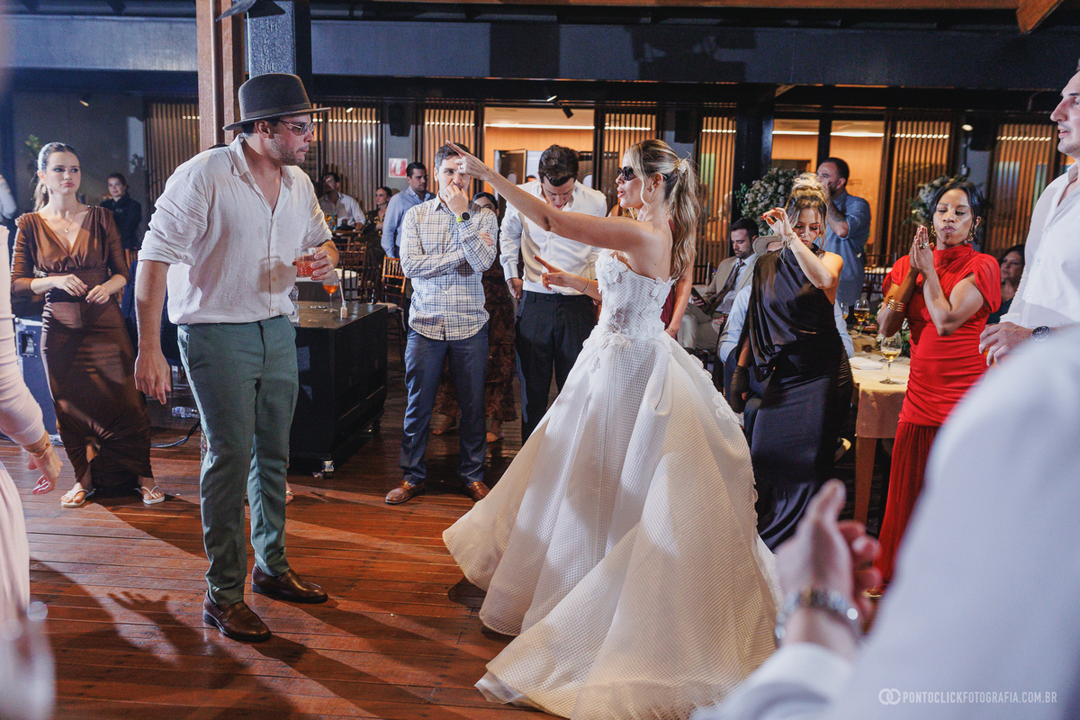 Noiva aponta para um convidado de chapéu enquanto dança na recepção do casamento. Fotógrafo de casamento Pontoclick Fotografia.