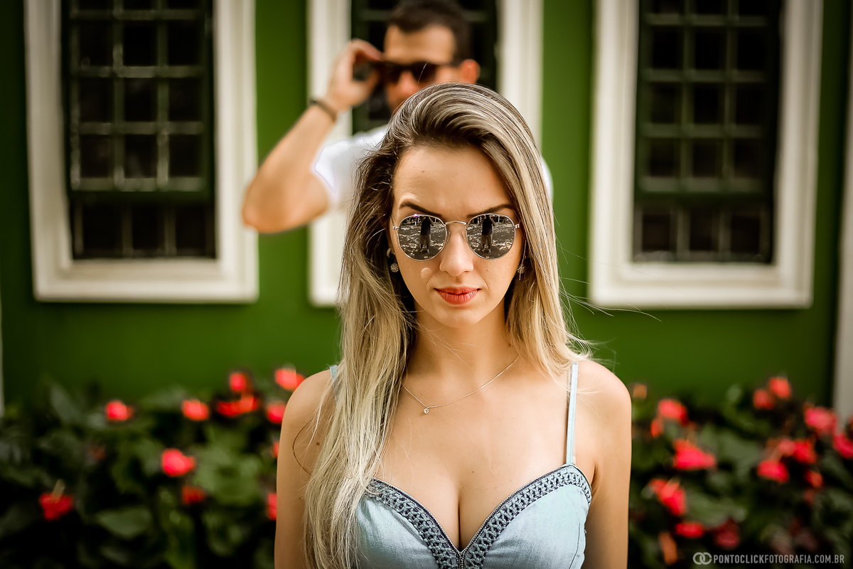 noiva loira na esta na frente do noivo ao fundo segurando o oculos de sol e no fundo um mural colorido em holambra