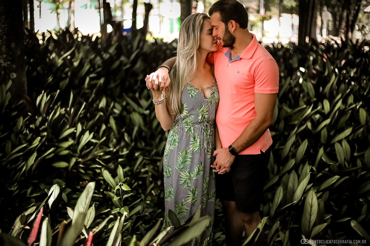 casal no meio de plantas rasteiras o noivo esta com a mao por cima do ombro da noiva e eles estao se beijando