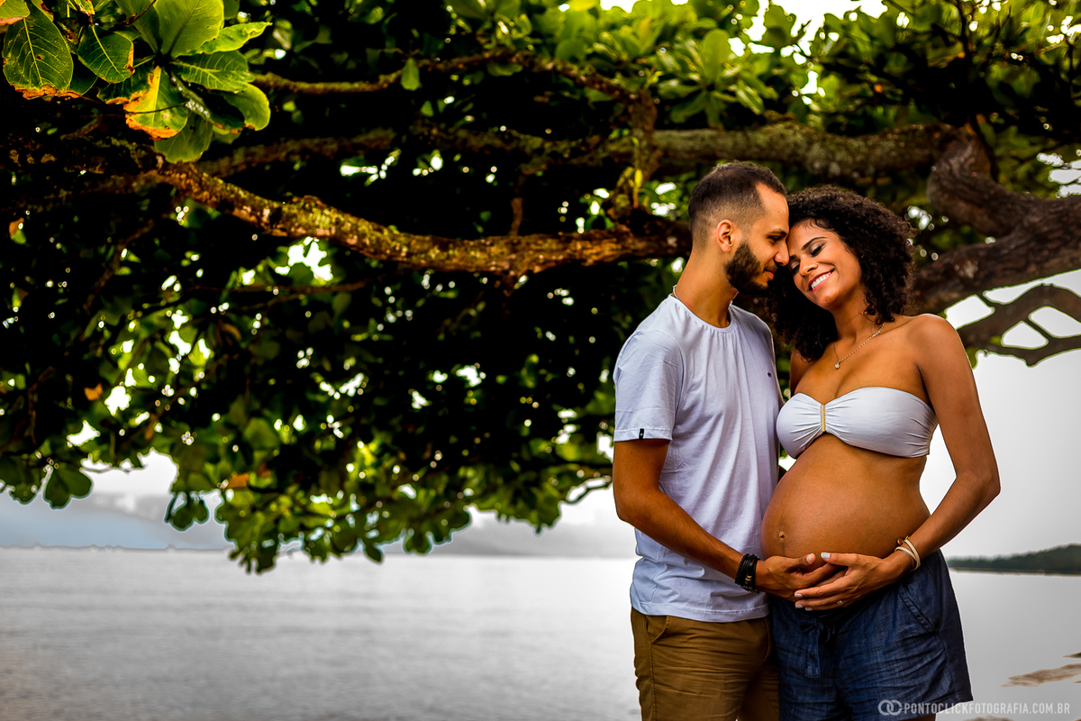 casal segurando a barriga da mamae gestante na praia de ilhabela