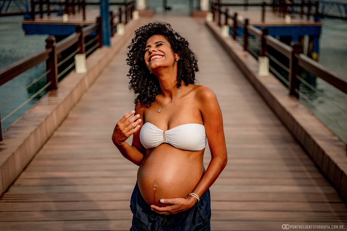 mamae gestante segurando a barriga e sorrindo no pier em ilhabela